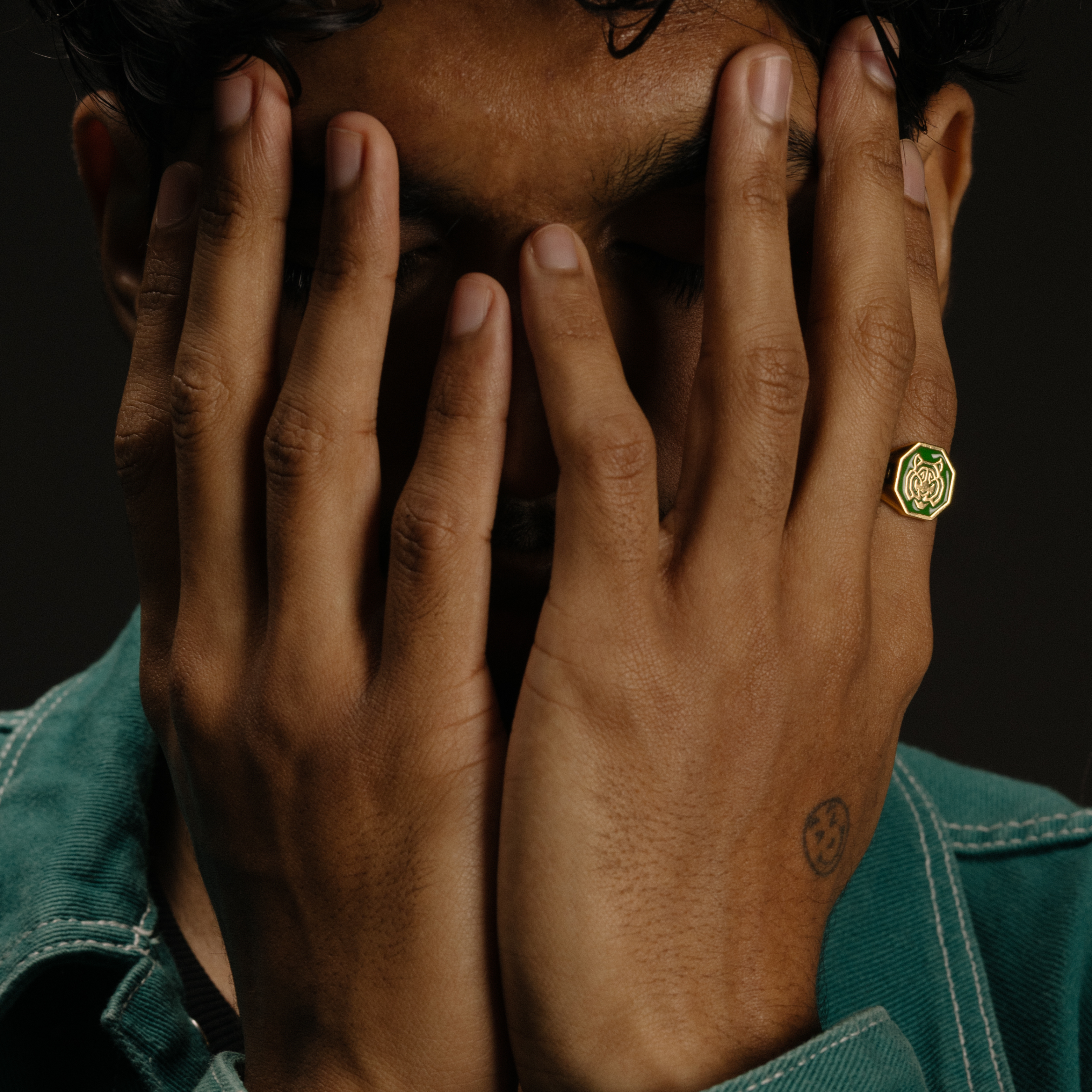 Men’s gold tiger signet ring with green enamel worn on hand